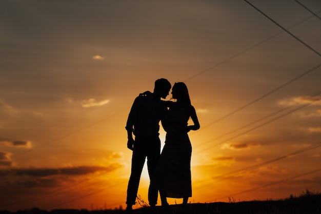 Silhouette of loving couple standing riverside. Couple against the beautiful sunset sky.