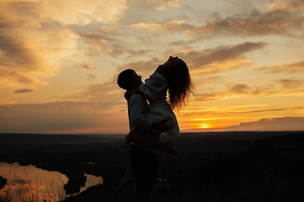 Silhouette of loving couple together outdoor in mountains over scenic sunset sky surface.