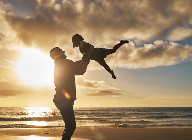 Silhouette of a loving father holding up his little child on the beach Parent spending time with their daughter while on holiday Happy little girl playing and bonding with her dad on vacation