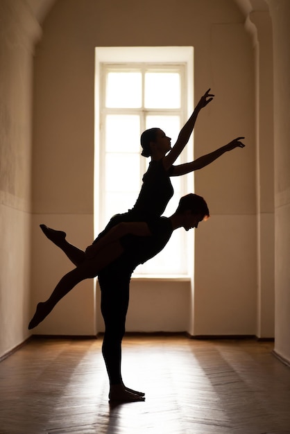 Silhouette of male and female dancers performing difficult artistic moves in corridor of theatre Dancers performing together