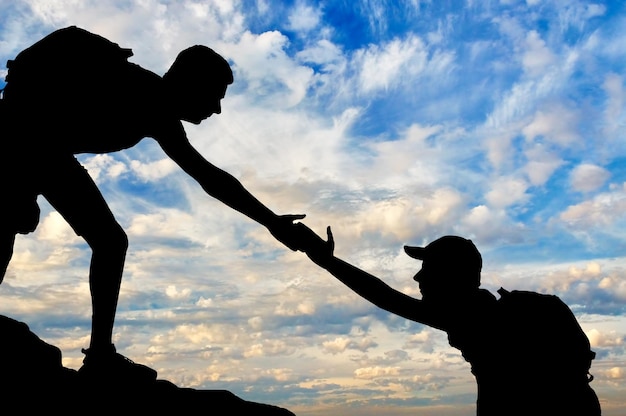 Silhouette of a male mountaineer giving a helping hand to his partner. The concept of teamwork