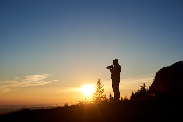 Silhouette of male photographer with photo camera at sunrise