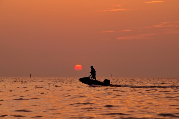 Silhouette of man driving jetski on the sea with during sunset