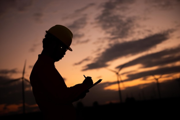 Silhouette of man engineer working and holding the report at wind turbine farm Power Generator Station on mountainThailand people