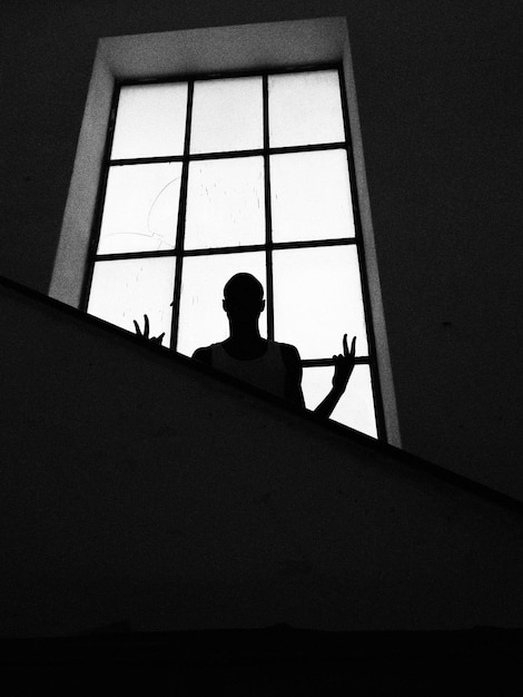 Photo silhouette man gesturing victory sign against window