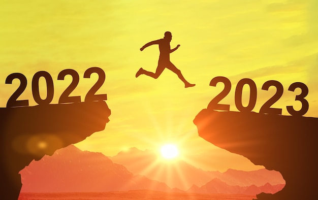 Silhouette man jump between 2022 and 2023 years over sun and through on gap of hill evening sky Welcome Happy New Year 2023 Symbol of starting and welcome happy new year 2023