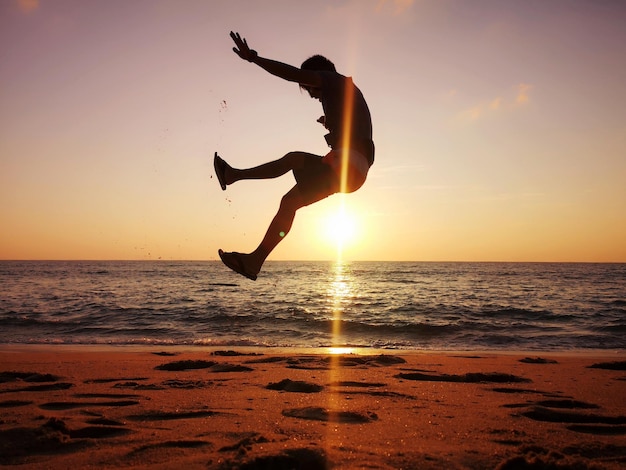 Photo silhouette man jumping at beach against sky during sunset