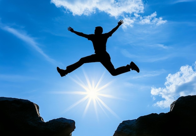 Photo silhouette of a man jumping over a gap between two rocks with a bright sun shining in the sky