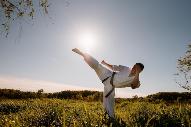 A silhouette of man karate fighter in white kimono high kick on the sunset background