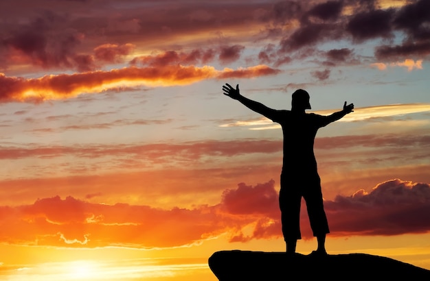 Silhouette of a man on a mountain top on sunset sky background