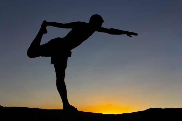 Silhouette of man practicing yoga at sunset on a rock in nature. Backlight. Copy space.