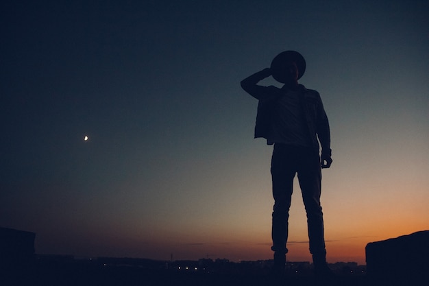 Silhouette of a man's , watching the sunset over the city. Urban man with hat. Good looking.