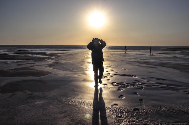 Photo silhouette man standing on beach against sky during sunset