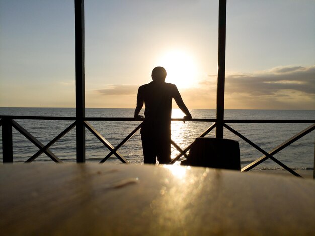 Photo silhouette man standing by sea against sky during sunset