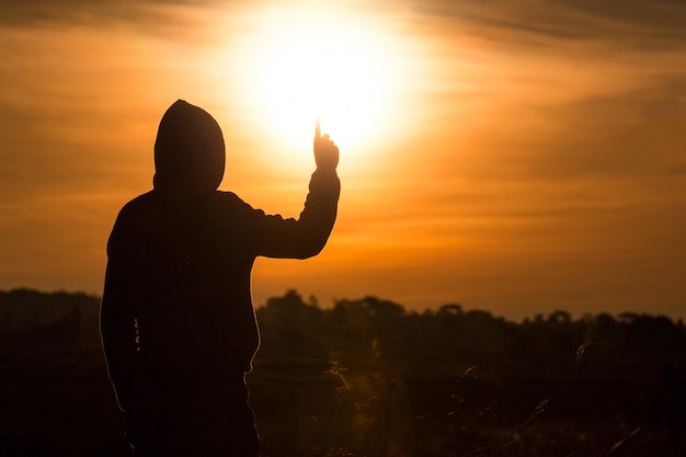 Silhouette of a man standing and rise his hands up in the air during sunset