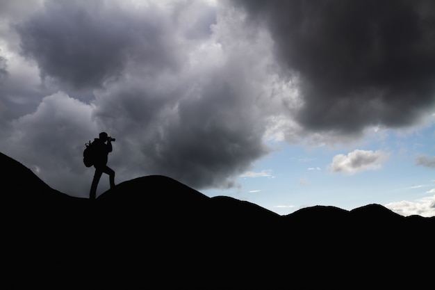 Silhouette of a man with backpack in the mountains is taking pictures of the landscape