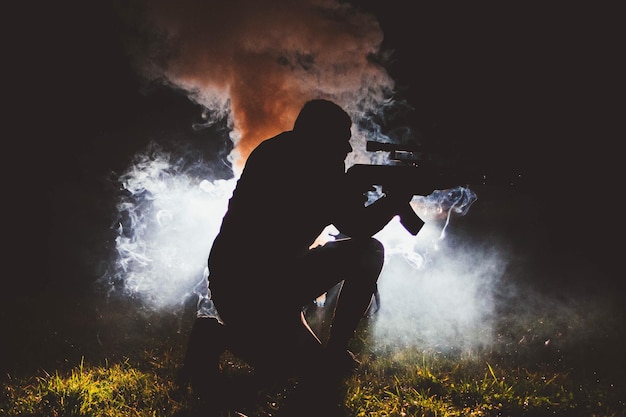 Photo silhouette man with weapon kneeling on field at night