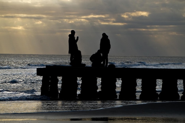 Silhouette men standing on beach against sky during sunset