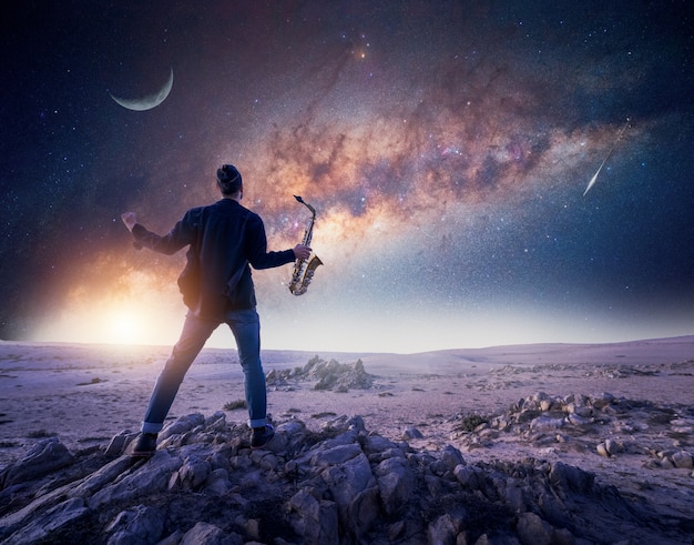 silhouette of a musician or saxophonist with open arms on a rock under the Milky Way