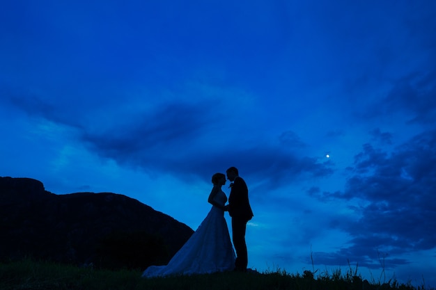 Silhouette of the newlyweds against the sky at sunset wedding