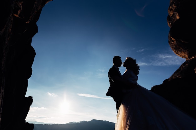 Silhouette of newlyweds hugging each other on a background of cliffs and mountains