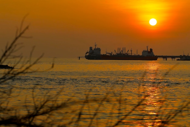 Silhouette off shore oil tanker ship in the middle of the sea at full sunset time