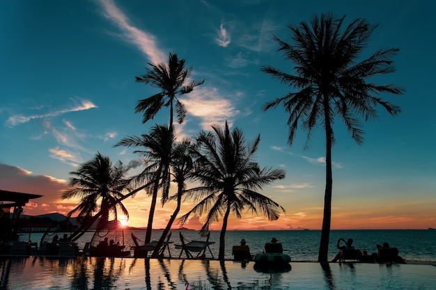 Silhouette palm tree and group of tourist looking at sunset over the sea.