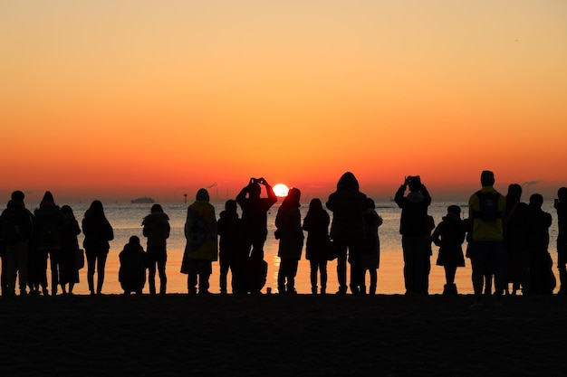 Silhouette people at beach against orange sky