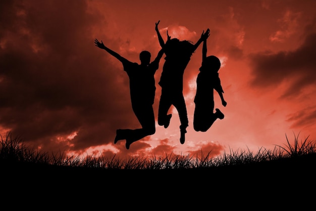 Silhouette of people jumping against red sky over grass