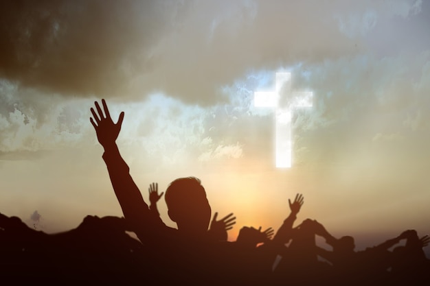 Silhouette of people looking at Christian cross with a sunset sky background