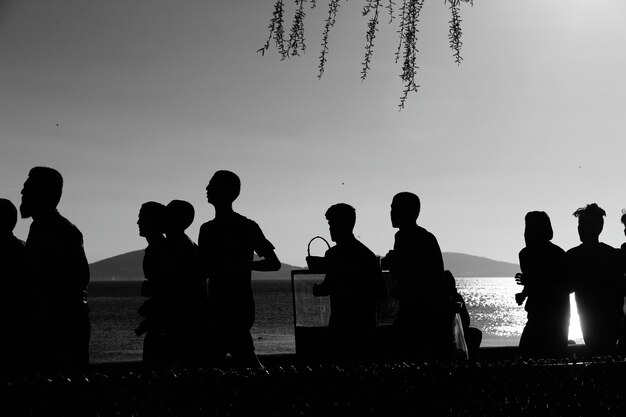 Photo silhouette people standing by lake against clear sky