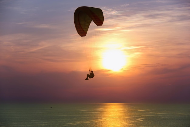 Silhouette of person in parachute at sunset over sea in Phuket Thailand Man paragliding at dusk