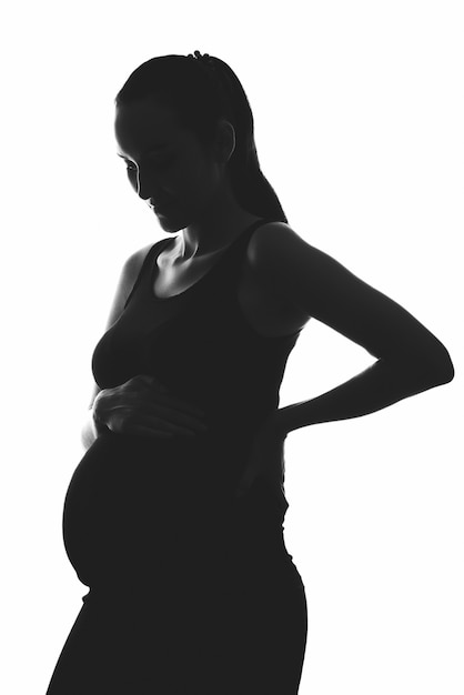 Silhouette portrait of pregnant woman on white background with hands on belly, vertical image, ivf pregnancy concept