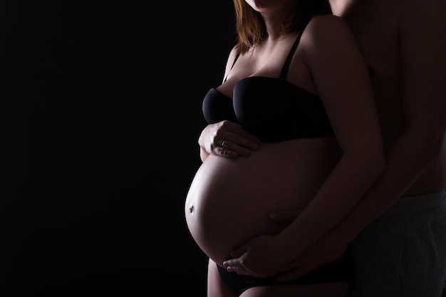 Silhouette of pregnant woman posing in lingerie with husband over black background