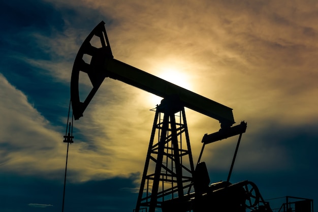 Silhouette of a pumpjack with piston pump on an oil well against the background of an alarming sky