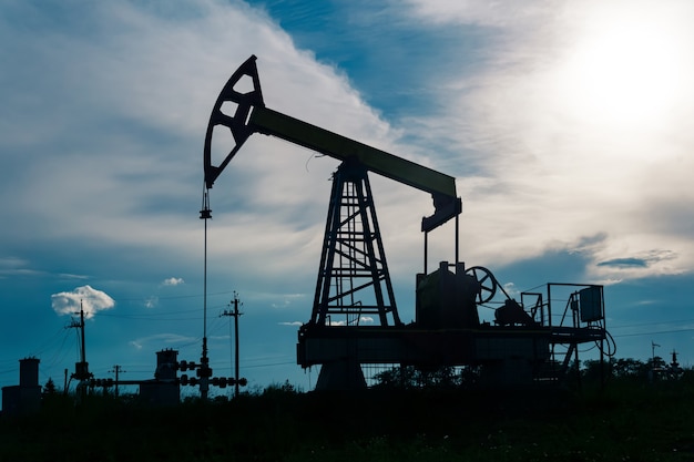 Silhouette of a pumpjack with piston pump on an oil well against the background of sky