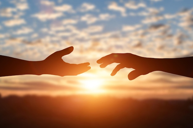 Silhouette of reaching giving a helping hand hope and support each other over sunset background Help friendship international day concept