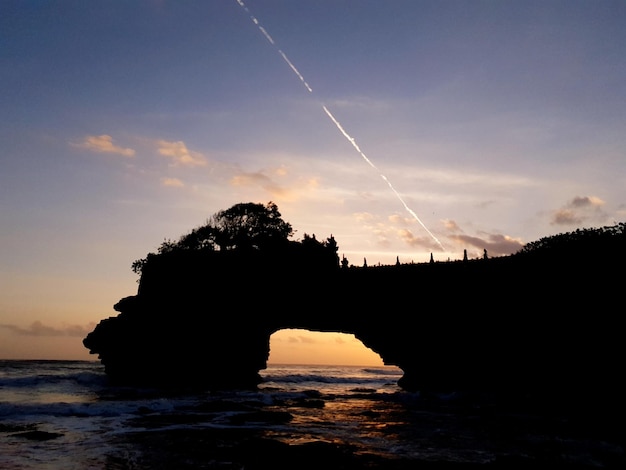 Photo silhouette rocks by sea against sky during sunset