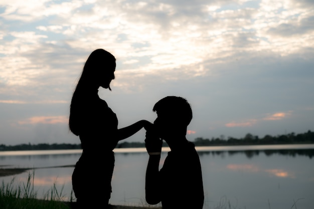 The silhouette of a romantic couple standing, hugging each other and watching the sunset. Romance and love concept.