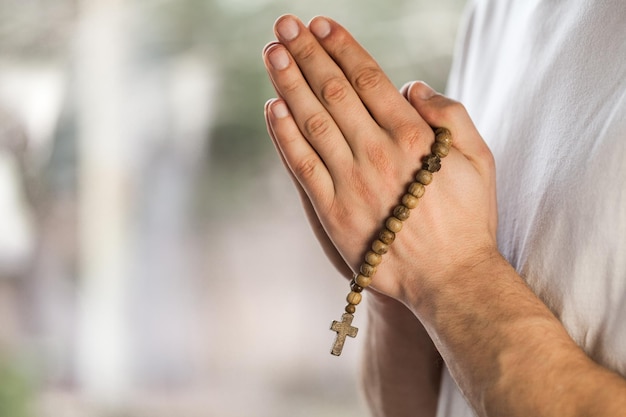 Silhouette rosary against cross in hand. Background sunrise