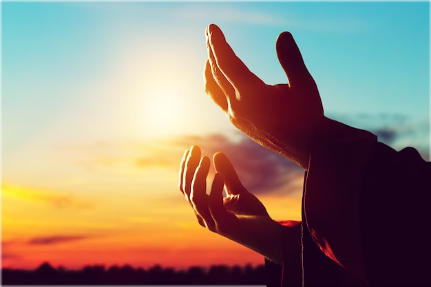 Silhouette rosary against cross in hand