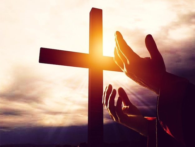 Silhouette rosary against cross in hand