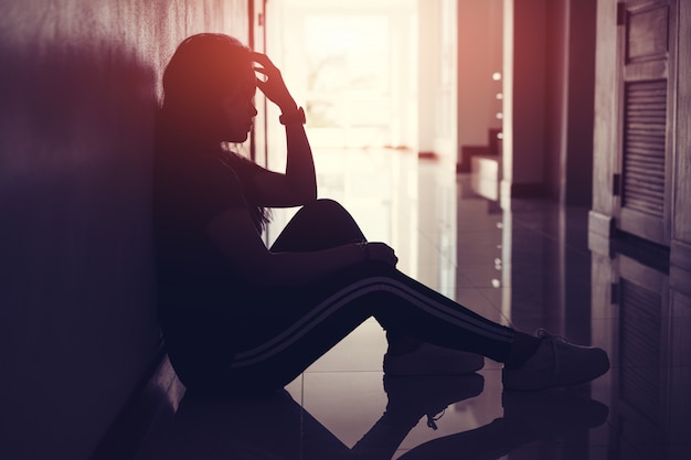 Silhouette of sad and depressed women sitting at walkway of condominium or office with backlit and lens flare