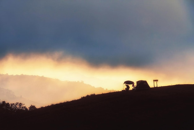 Silhouette scene of mountain man camping in misty morning