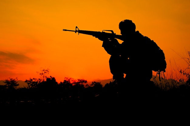 Silhouette shot of soldier holding gun with colorful sky and  mountain in background