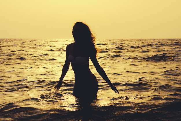 Silhouette of a slender woman in the water at the beach in sunshine