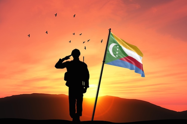 Silhouette of a soldier with the Comoros flag stands against the background of sunset or sunrise