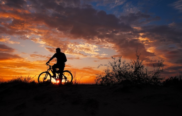 Silhouette of sports person cycling on the meadow on the beautiful sunset.  