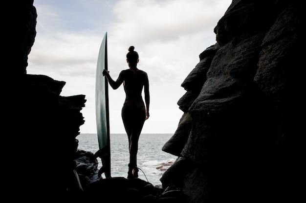 Silhouette sporty girl in the swimsuit standing with the surf between the rocks on the beach Atlantic ocean