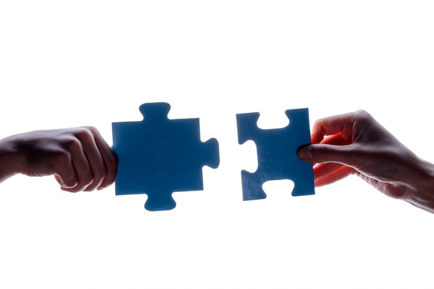 Silhouette of two hand holding couple of blue jigsaw puzzle piece on white 